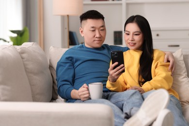 Happy couple with smartphone on sofa at home