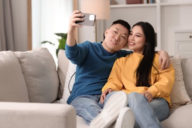 Happy couple taking selfie on sofa at home