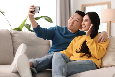 Happy couple taking selfie on sofa at home