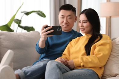 Happy couple with smartphone on sofa at home