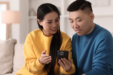Happy couple with smartphone on sofa at home