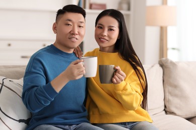 Happy couple with cups of drink on sofa at home