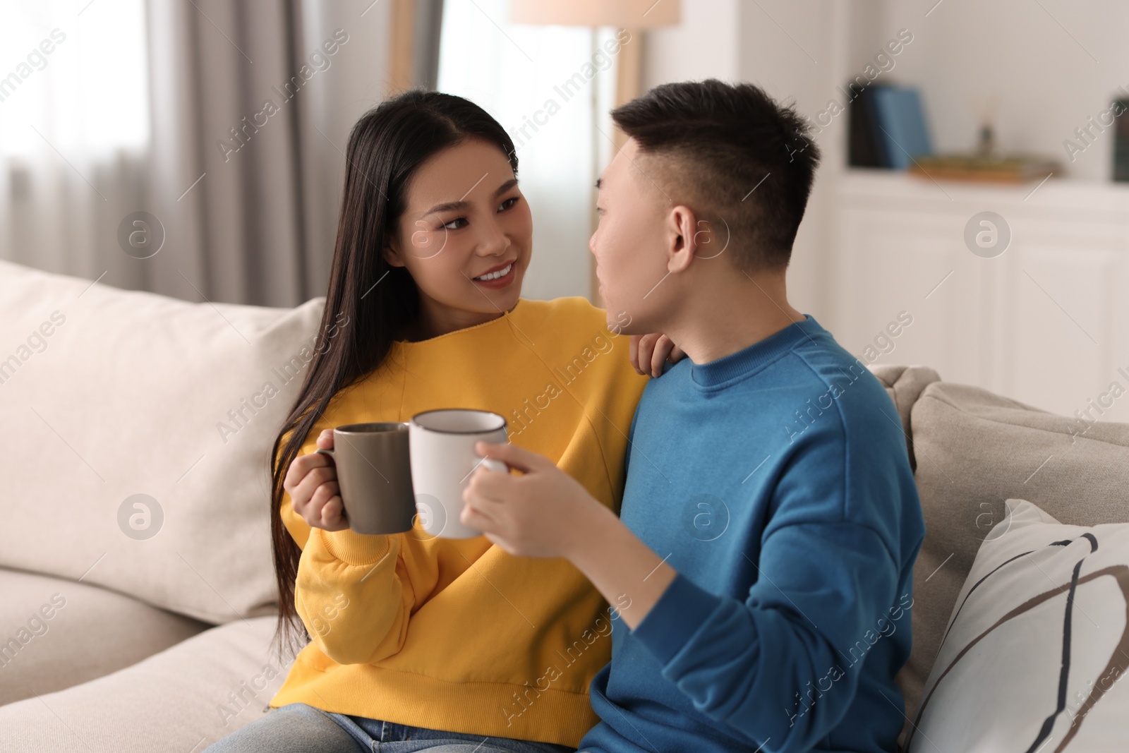 Photo of Happy couple with cups of drink on sofa at home