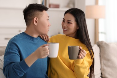 Happy couple with cups of drink on sofa at home