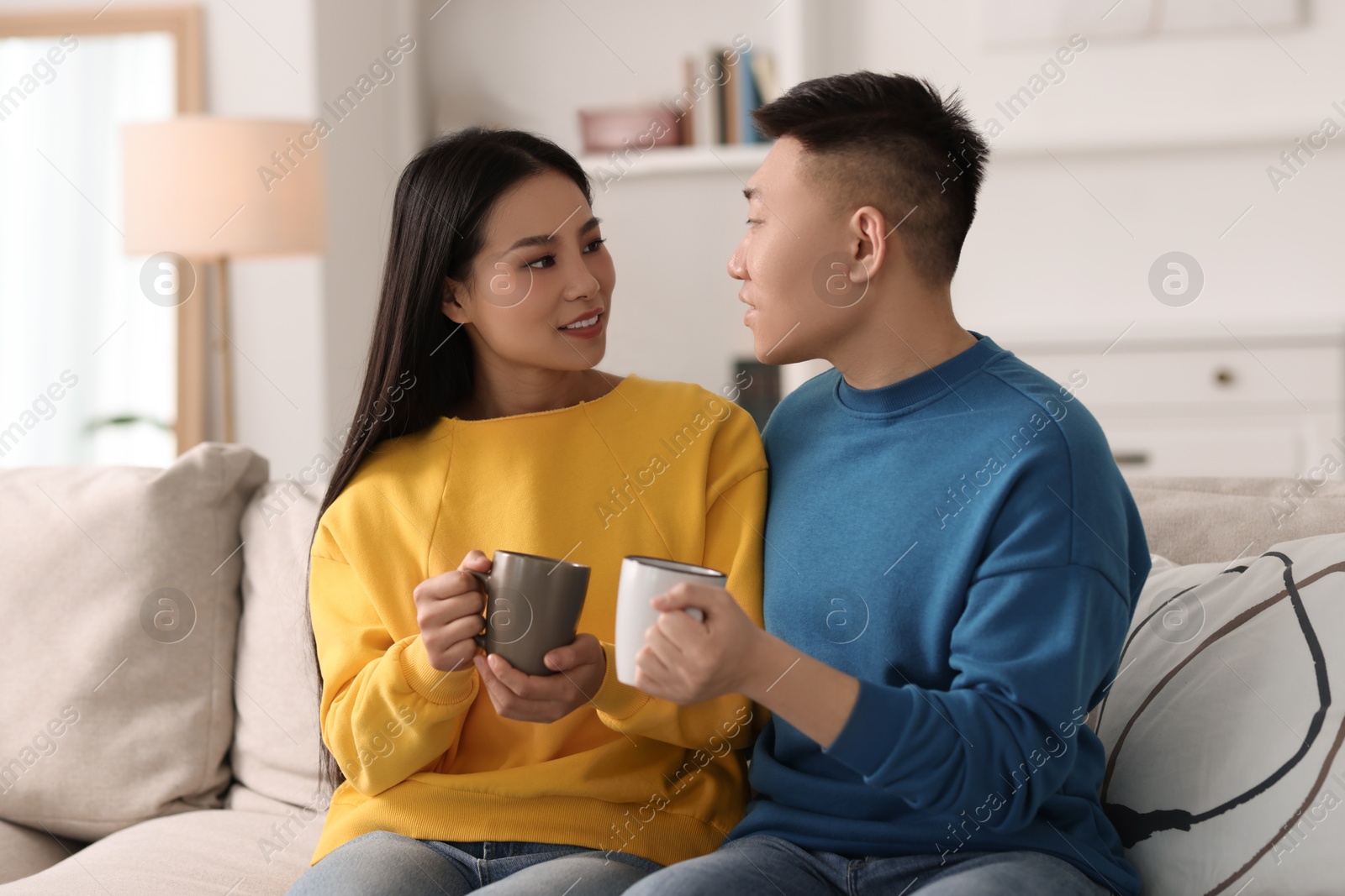 Photo of Happy couple with cups of drink on sofa at home