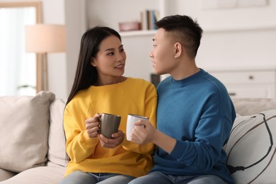 Happy couple with cups of drink on sofa at home