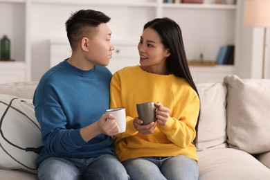 Photo of Happy couple with cups of drink on sofa at home