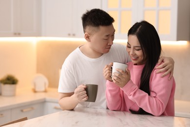 Lovely couple with cups of drink enjoying time together in kitchen, space for text