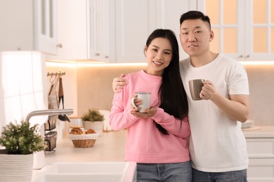 Lovely couple with cups of drink enjoying time together in kitchen