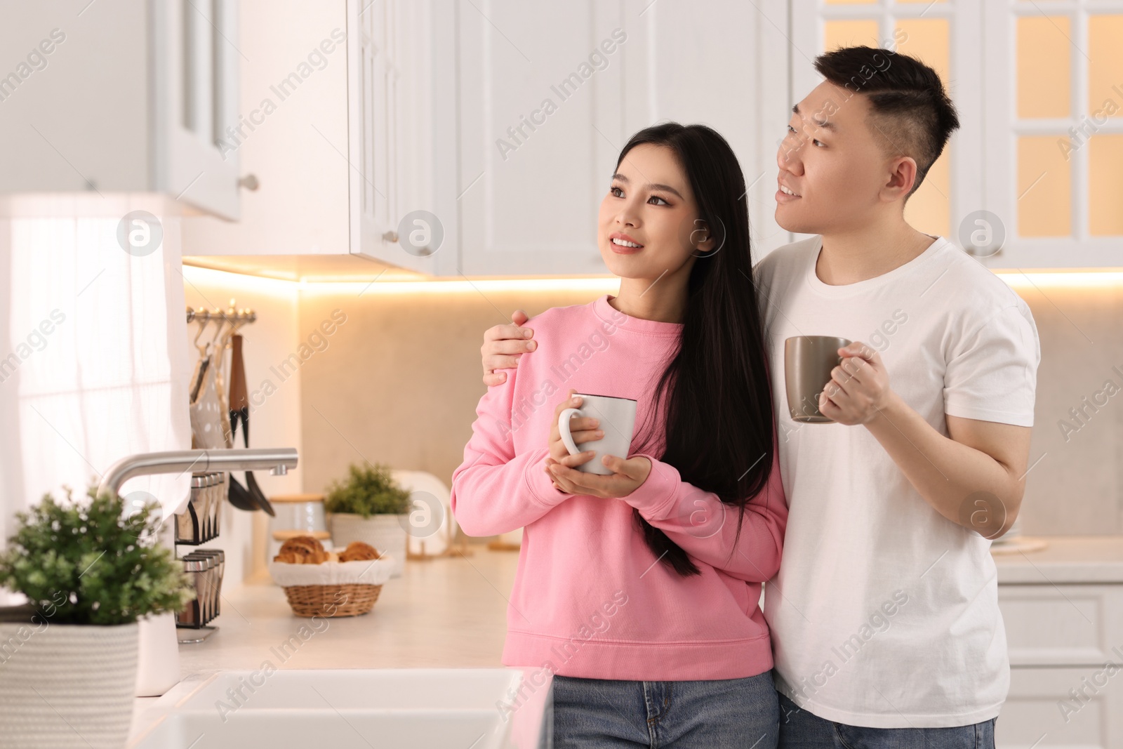 Photo of Lovely couple with cups of drink enjoying time together in kitchen