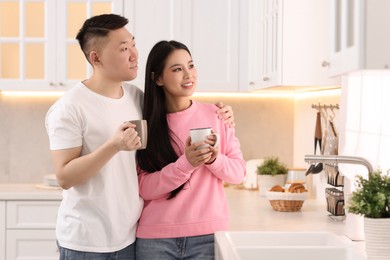 Lovely couple with cups of drink enjoying time together in kitchen