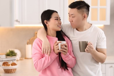 Lovely couple with cups of drink enjoying time together in kitchen