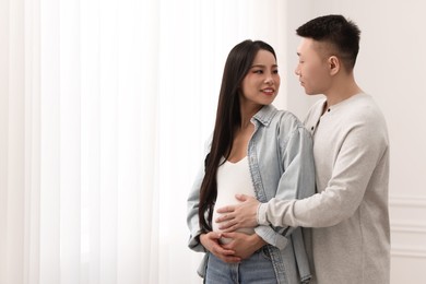 Man touching his pregnant wife's belly at home, space for text