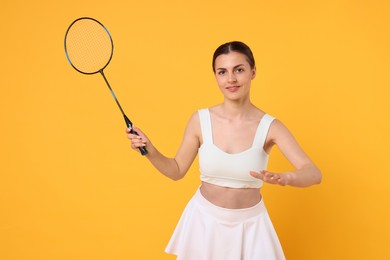 Young woman with badminton racket on orange background