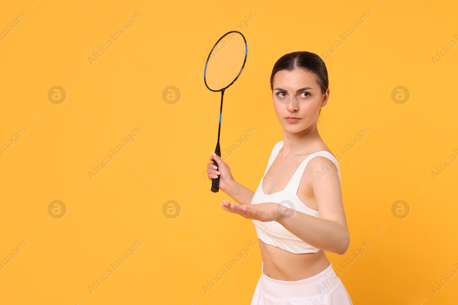 Photo of Young woman with badminton racket on orange background, space for text