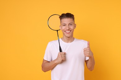 Young man with badminton racket on orange background