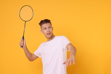 Young man with badminton racket on orange background