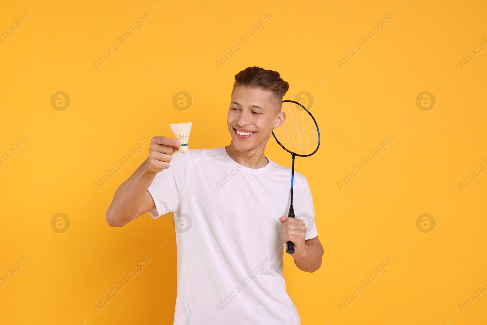 Photo of Young man with badminton racket and shuttlecock on orange background