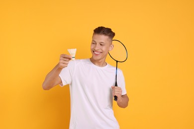 Photo of Young man with badminton racket and shuttlecock on orange background