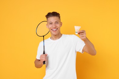 Young man with badminton racket and shuttlecock on orange background