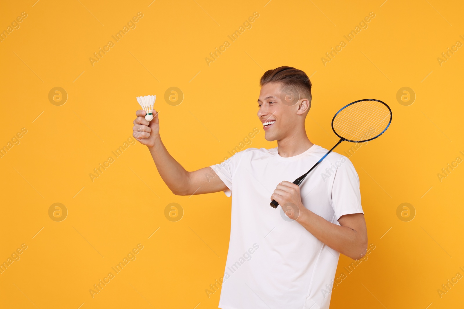 Photo of Young man with badminton racket and shuttlecock on orange background