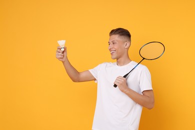 Photo of Young man with badminton racket and shuttlecock on orange background