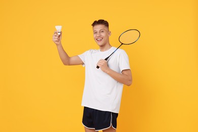 Photo of Young man with badminton racket and shuttlecock on orange background