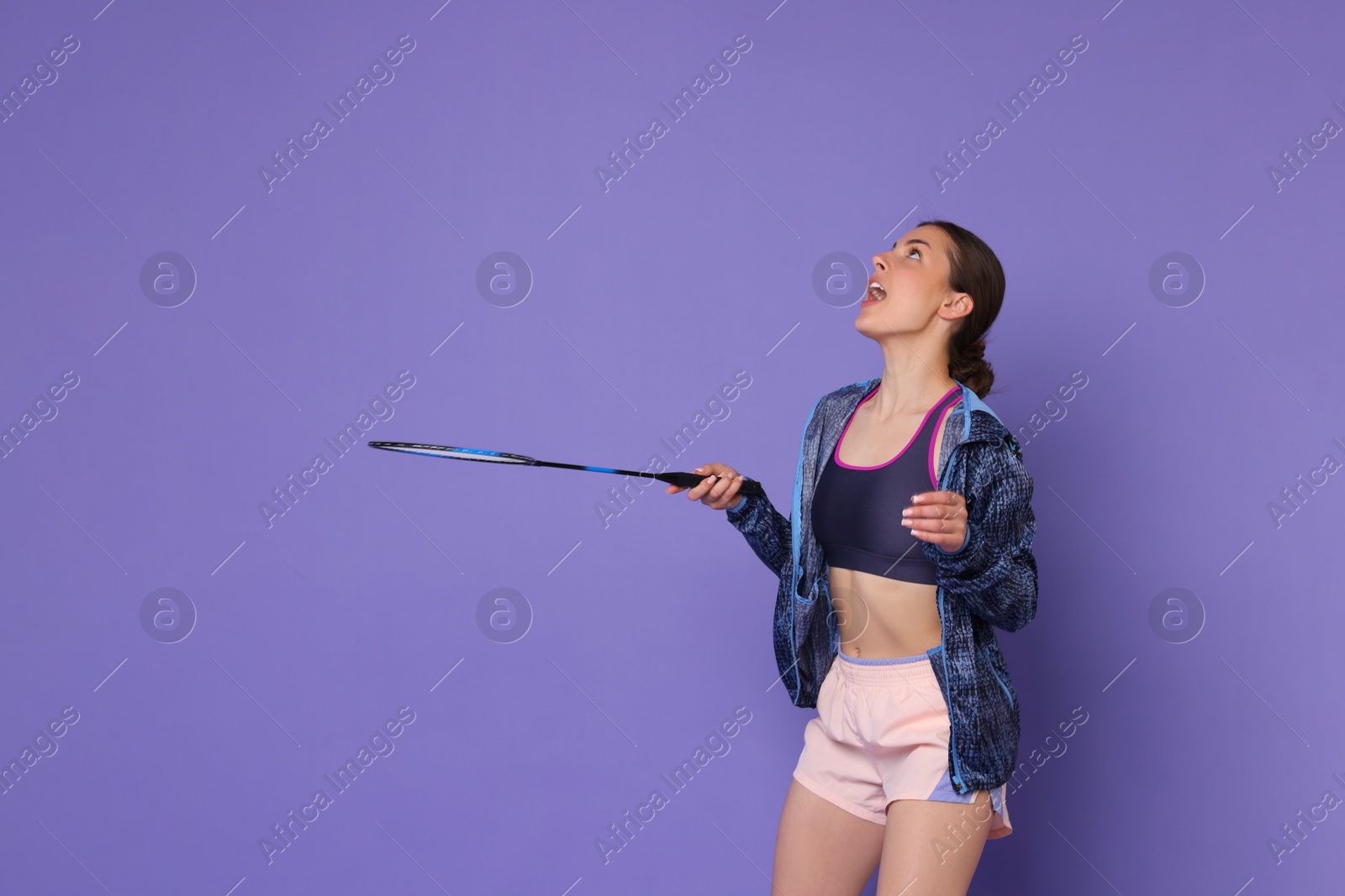 Photo of Young woman with badminton racket on purple background, space for text