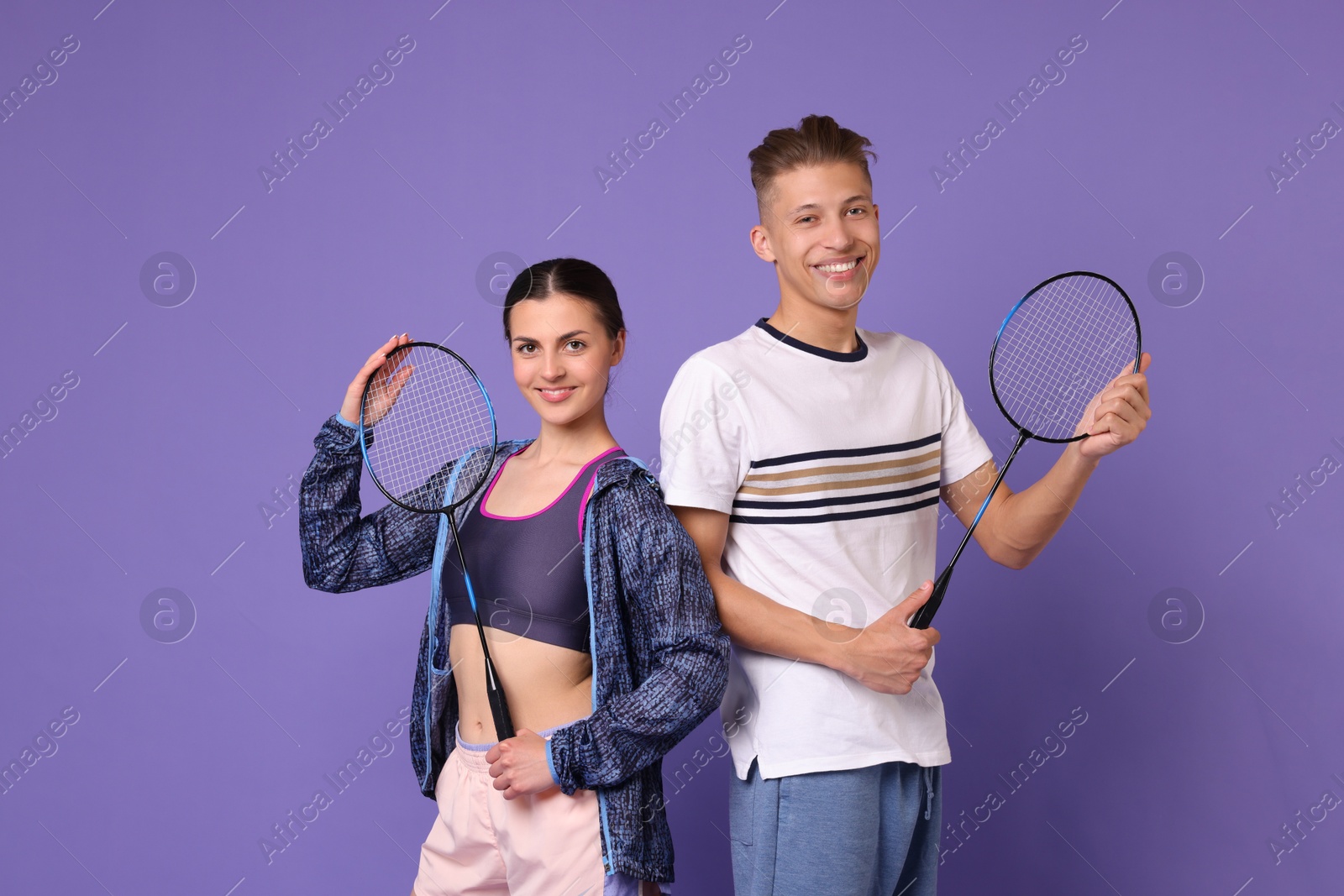 Photo of Young man and woman with badminton rackets on purple background