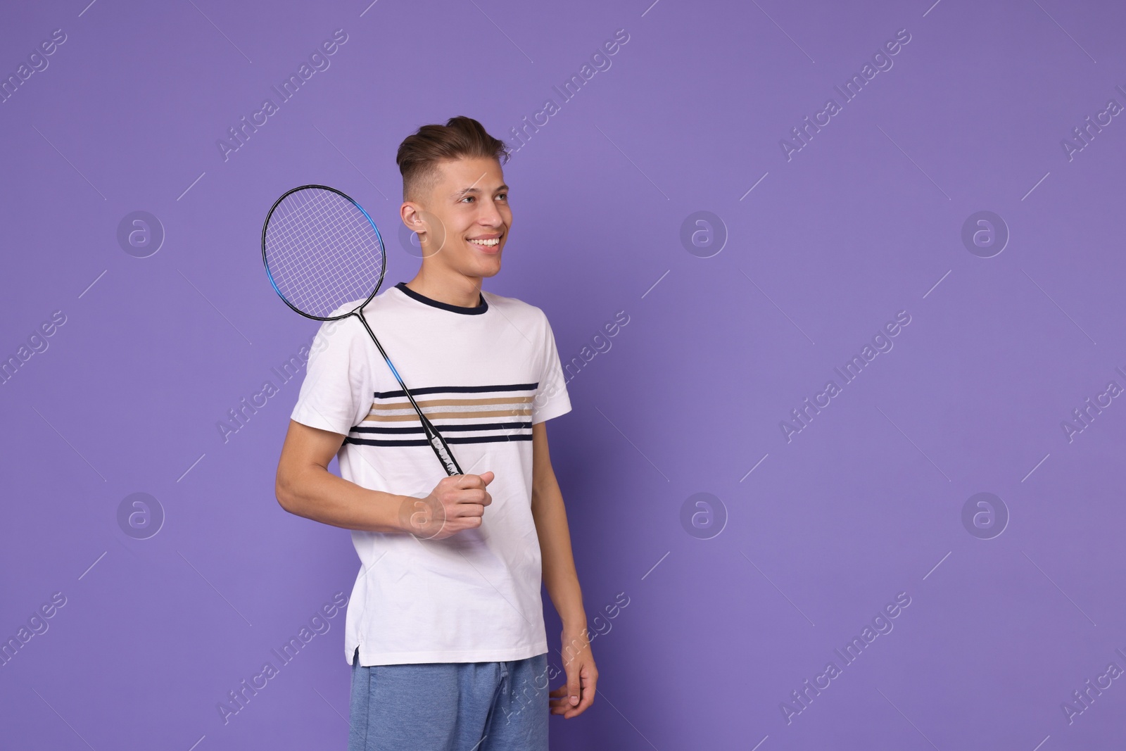 Photo of Young man with badminton racket on purple background, space for text