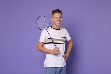Young man with badminton racket on purple background
