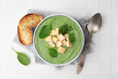 Photo of Delicious spinach cream soup with croutons served on white tiled table, flat lay