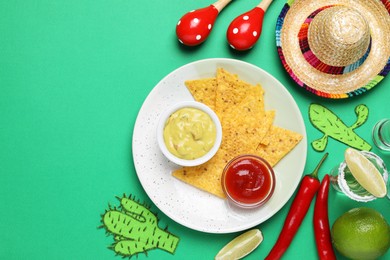 Flat lay composition with nachos chips and Mexican sombrero hat on green background, space for text