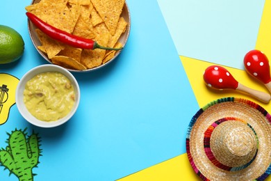 Mexican sombrero hat, maracas, guacamole, nachos chips, chili and paper cactus on color background, flat lay. Space for text