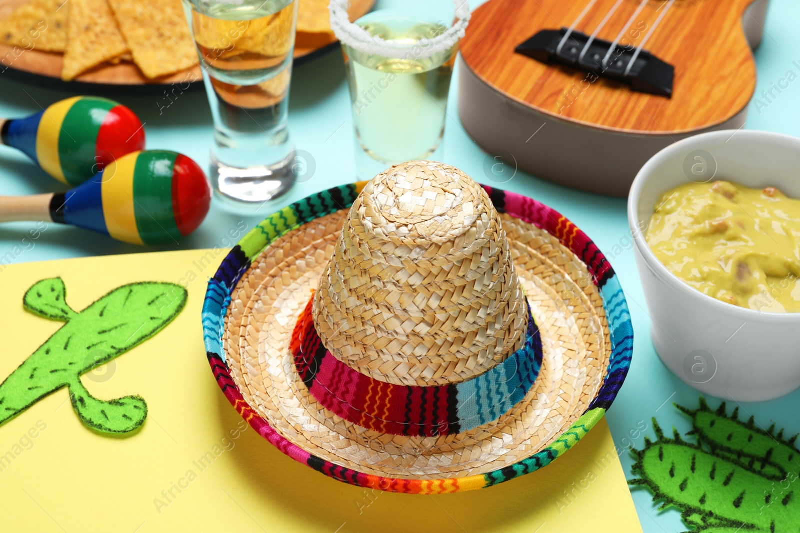 Photo of Mexican sombrero hat, guacamole, maracas, paper cactus and tequila on color background