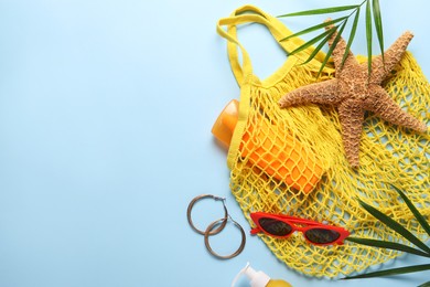 String bag, different beach accessories and palm leaves on light blue background, flat lay. Space for text