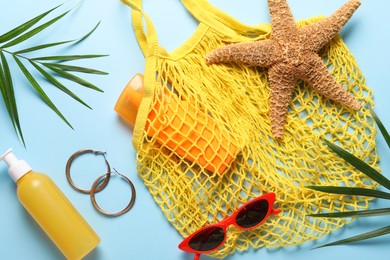 String bag, different beach accessories and palm leaves on light blue background, flat lay