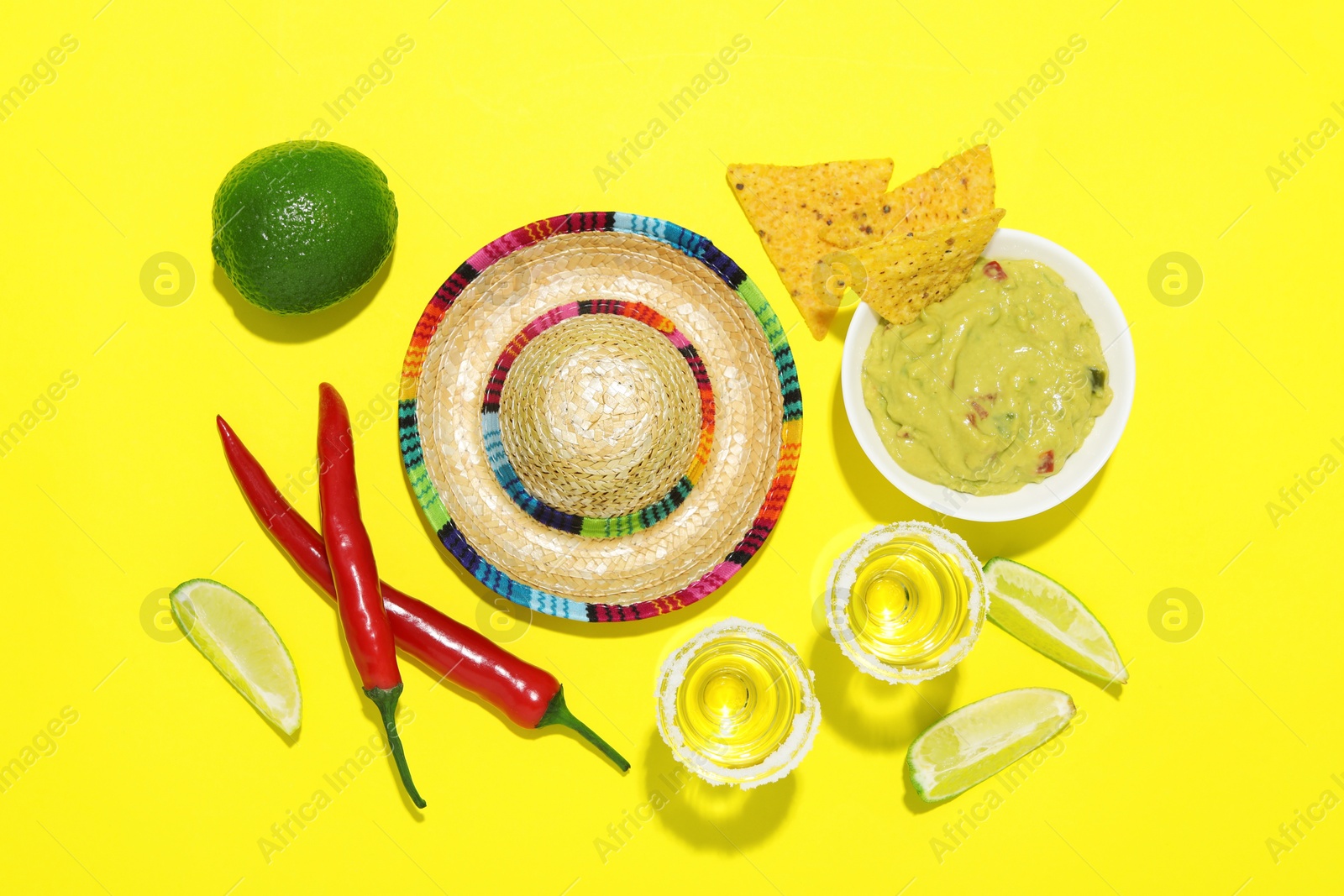 Photo of Mexican sombrero hat, tequila, nachos chips, guacamole and other products on yellow background, flat lay