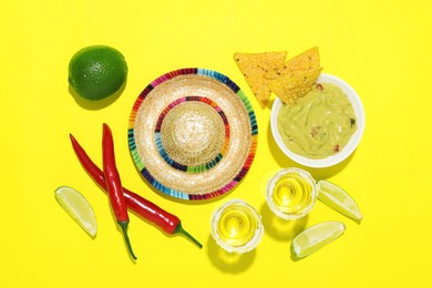 Mexican sombrero hat, tequila, nachos chips, guacamole and other products on yellow background, flat lay