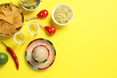 Mexican sombrero hat, tequila, nachos chips, guacamole and maracas on yellow background, flat lay. Space for text