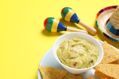 Nachos chips, guacamole, maracas and Mexican sombrero hat on yellow background, closeup. Space for text