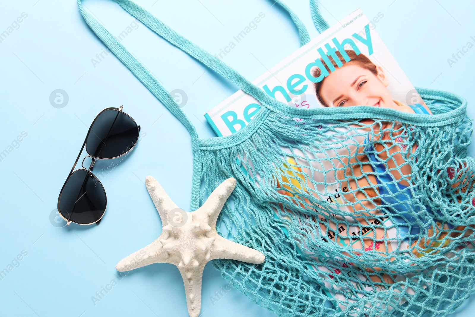 Photo of String bag, sunglasses, starfish and magazine on light blue background, top view