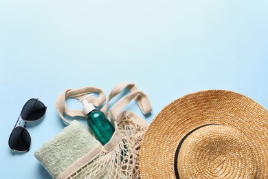 String bag, sunglasses, towel, straw hat and cosmetic product on light blue background, top view. Space for text