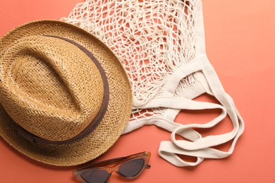 String bag, sunglasses and hat on coral background, top view