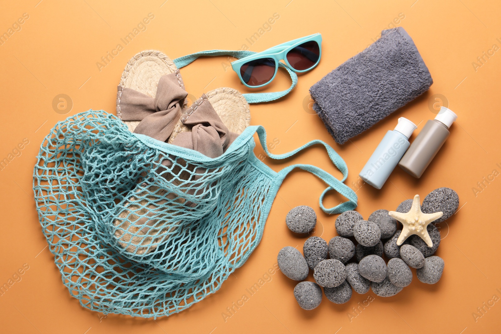 Photo of String bag and different beach accessories on pale orange background, flat lay