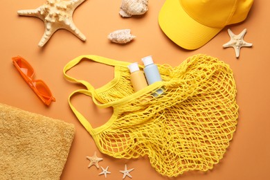 String bag and different beach accessories on pale orange background, flat lay