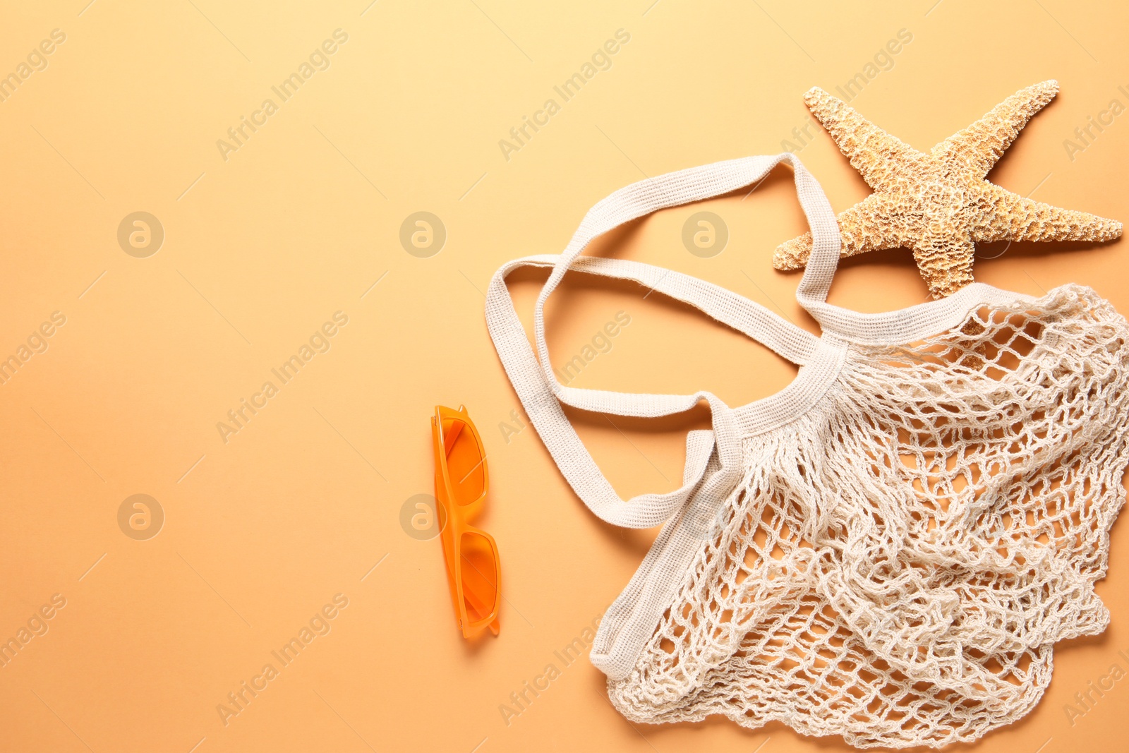 Photo of String bag, sunglasses and starfish on pale orange background, flat lay. Space for text