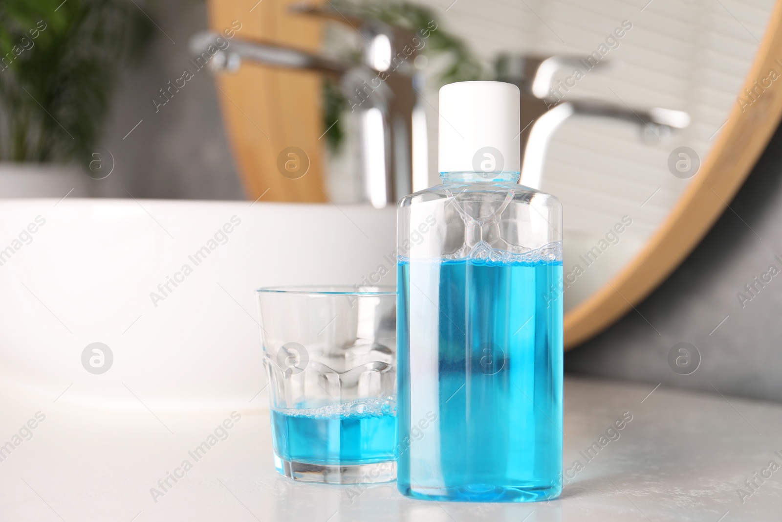 Photo of Bottle and glass of mouthwash on white countertop in bathroom