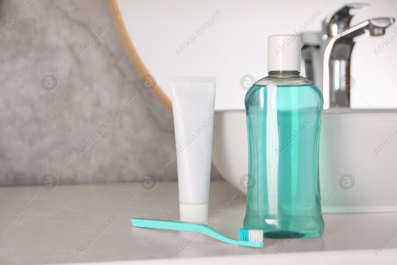 Photo of Bottle of mouthwash, toothpaste and toothbrush on light countertop in bathroom