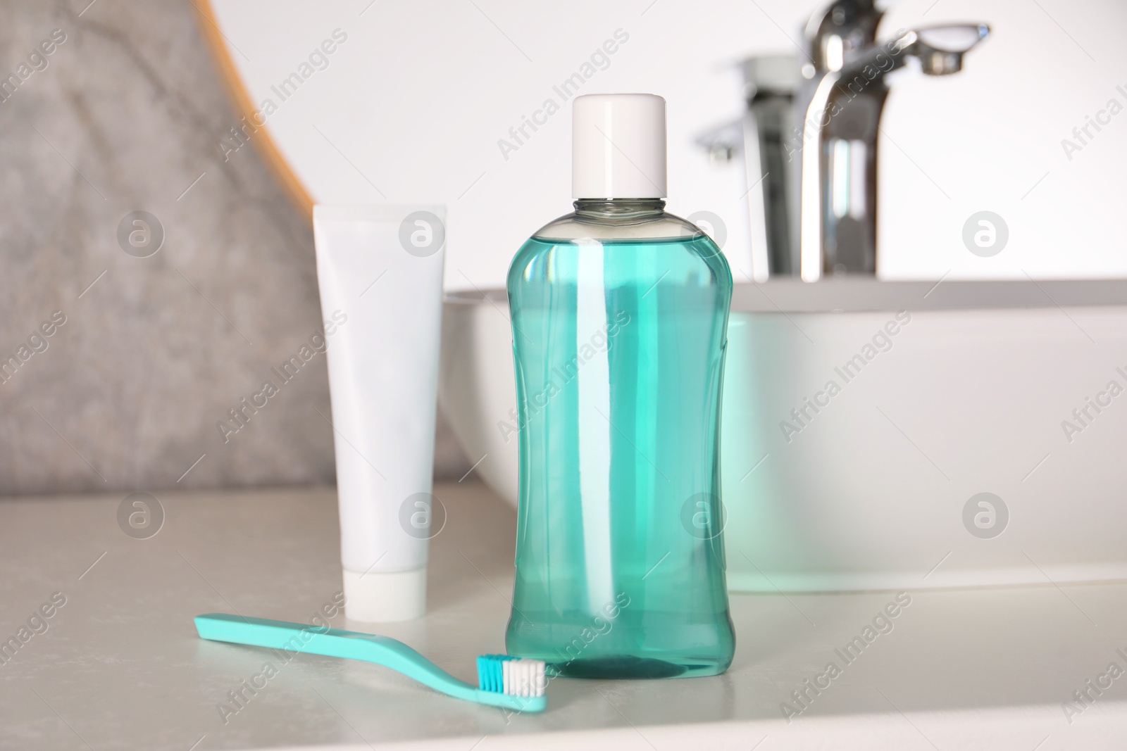 Photo of Bottle of mouthwash, toothpaste and toothbrush on light countertop in bathroom